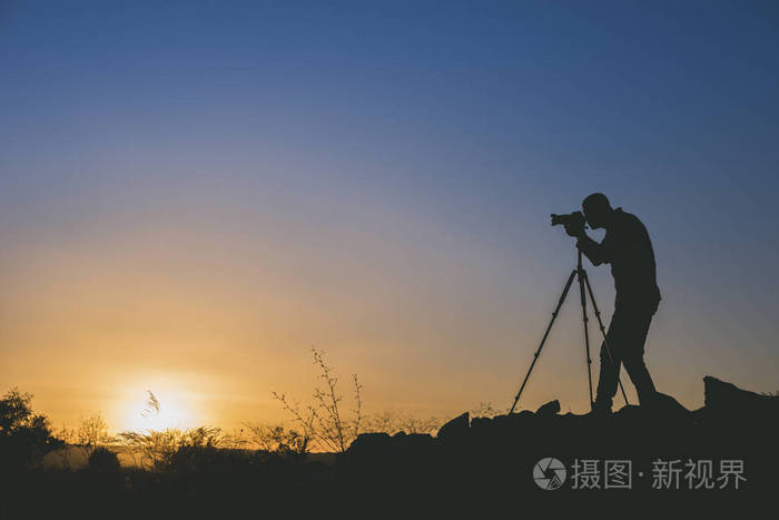 黑色摄影师在日落时拍照的剪影。具有复制空间的图像