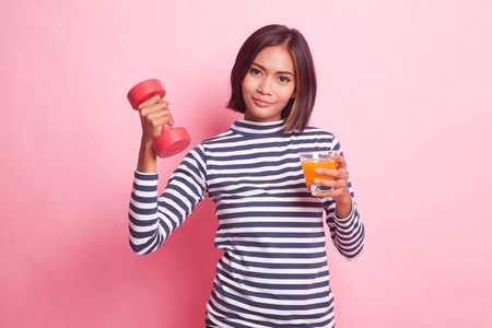 年轻的亚洲妇女与哑铃喝橙汁在粉红色的背景