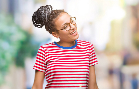年轻的编织头发非洲裔美国女孩戴眼镜在孤立的背景看着一边面带微笑, 自然的表情。笑自信
