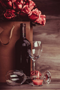 红酒瓶, 两杯葡萄酒, 木桌纸袋里的玫瑰。情人节庆祝概念。复制空间