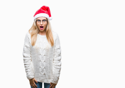 年轻美丽的金发女子戴着圣诞节帽子在孤立的背景害怕和震惊的惊讶的表情, 恐惧和兴奋的脸