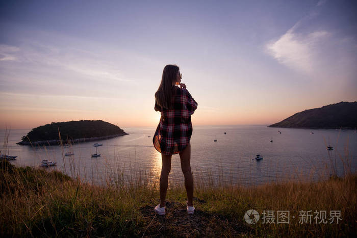 女性旅行者在日落时分看海上湾的背景山悬崖的边缘