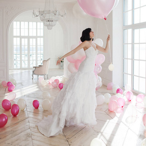 婚纱礼服在粉红色和白色的气球上的豪华室内苍蝇的年轻女子