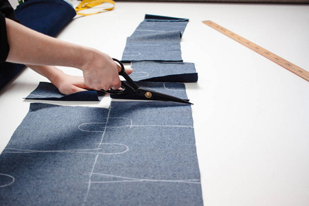 女裁缝用白色桌上的剪刀剪牛仔裤面料的手照片