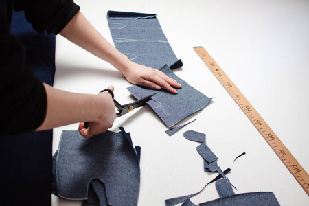 女裁缝用白色桌上的剪刀剪牛仔裤面料的手照片