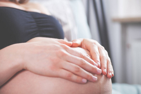 怀孕的女孩牵手心在家的肚子的形状