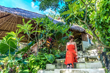 年轻时尚的女人穿着红色一个热带花园。幸福的女人放松在印度尼西亚巴厘岛上的肖像