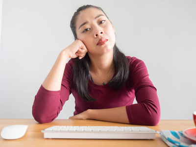 无聊和昏昏欲睡的亚洲妇女工作在她的办公桌上, 咖啡鼠标和键盘