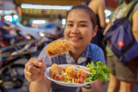 亚洲妇女享受吃炸的虾球 虾与柠檬和白菜切片把钱浪费在她手中的叉子。选择焦点在炒的虾球
