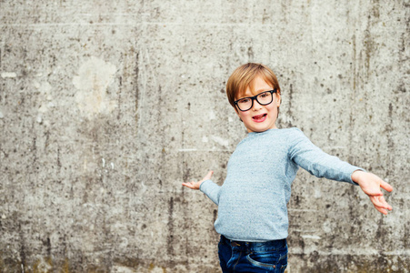 一个可爱的小男孩，戴着眼镜 淡蓝色套头衫和牛仔裤的室外肖像