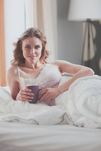 年轻女子躺在床上喝杯咖啡或茶