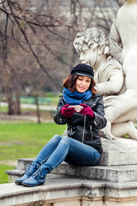 年轻的女性旅行者，让智能手机与丘比特雕像拍照春天的花园或公园中