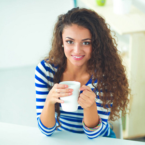 微笑的咖啡杯和笔记本电脑在家里的厨房里的年轻女子