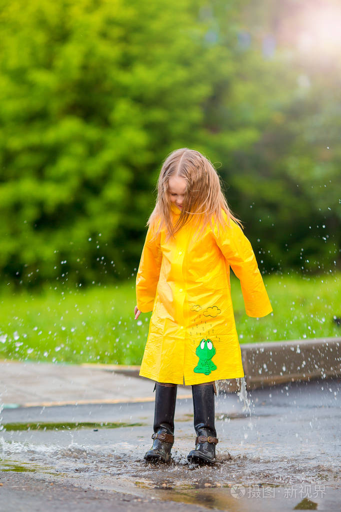 在雨衣和雨鞋在雨中在户外玩耍的小女孩