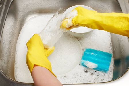 在对厨房的水槽洗玻璃的黄色手套的手