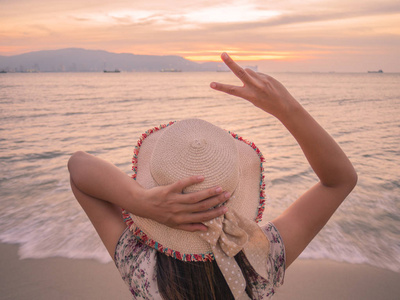 女人拥有两个手指或胜利的手势在海滩上在日落，显示鼓励当我们劝阻