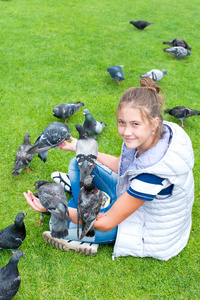 性格开朗的微笑女孩喂鸽子在夏天绿色公园