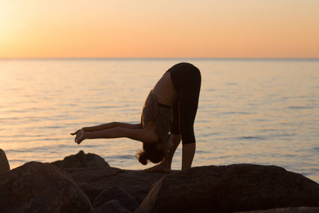 在瑜伽体式上早上海滩 漂亮合适的女人实践健身 exrxise 石头，早上大海或海洋背景健身混的血女人剪影