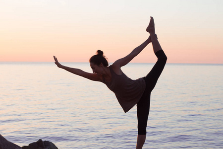 在瑜伽体式上早上海滩 漂亮合适的女人实践健身 exrxise 石头，早上大海或海洋背景健身混的血女人剪影