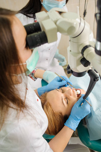 女牙医治疗龋在牙医办公室使用显微镜
