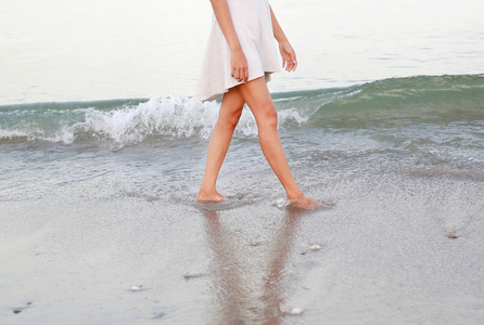 独自走在沙滩上的白色连衣裙的年轻女子
