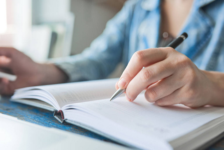 在笔记本中写女性手用蓝笔写单词写活动着一支笔和一本书与早上照明