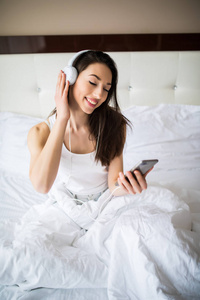 幸福的女人或十几岁的女孩在耳机从智能手机听音乐，跳舞，在家里的床上