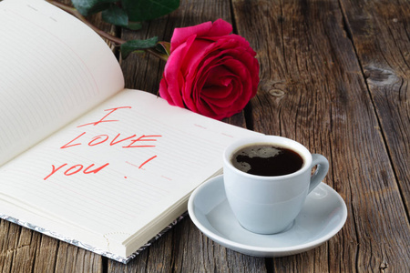 爱信记事本 红玫瑰和木桌上的咖啡杯。情人节的概念