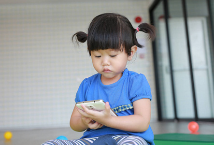 关闭了可爱的小亚洲宝贝女孩年龄约一岁和九个月，在孩子的房间玩智能手机