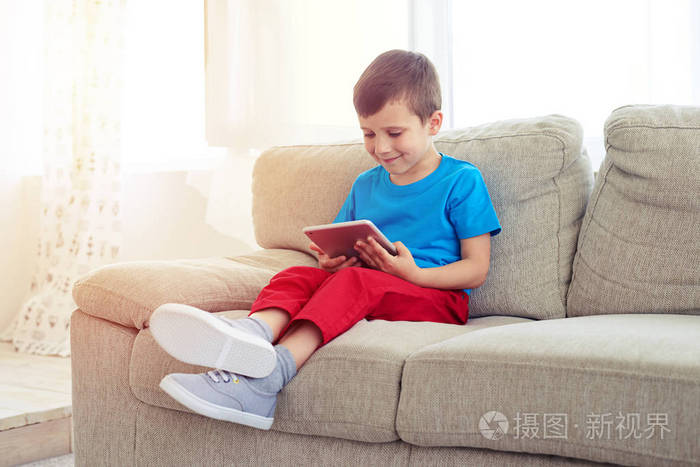 小男孩坐在沙发上与平板电脑的侧视图
