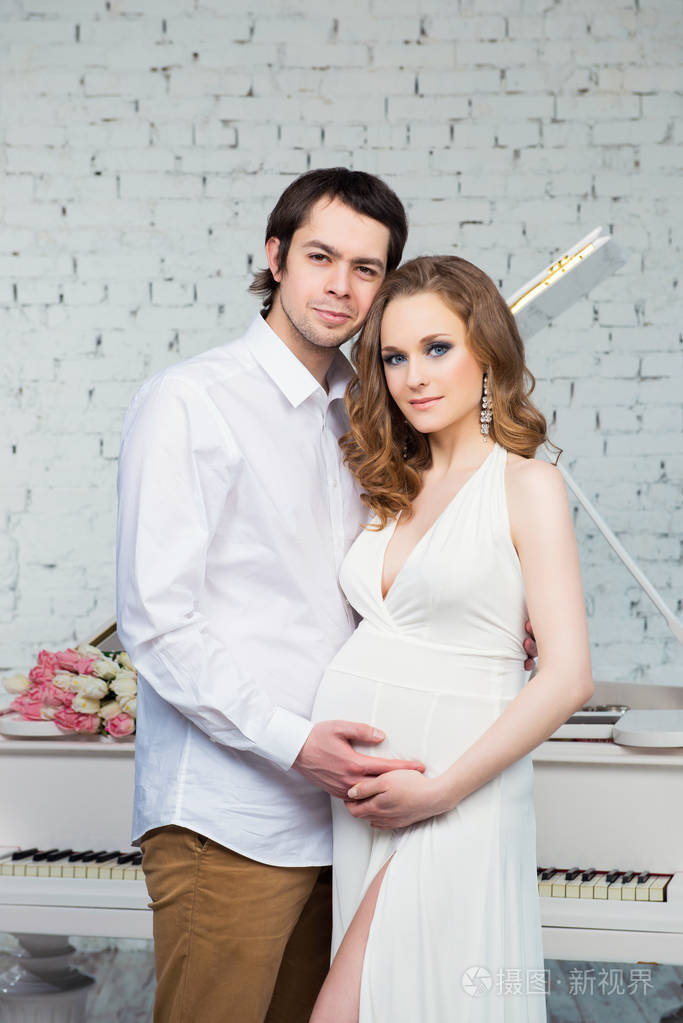 美丽的夫妇, 怀孕的年轻女人和男人拥抱着钢琴背景的爱照片-正版商用