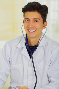 年轻英俊的笑脸医生用听诊器在他脖子上，反对势力的相机，在一名医生，咨询室背景