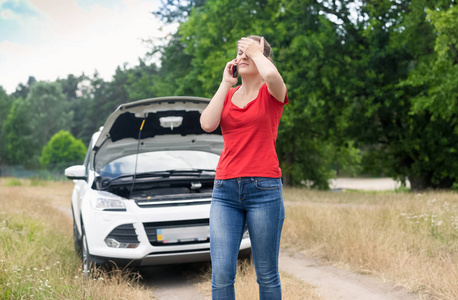 悲伤的女人站在破车，并呼吁他在手机上