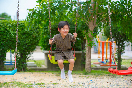 合乐亚洲男孩穿日本布玩秋千在公园里