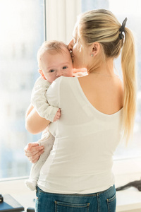 美丽的母亲拥抱她 3 个月大男婴在窗口