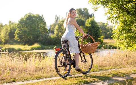 美丽的年轻女子骑着自行车在河边在炎热阳光明媚