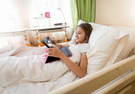 十几岁的女孩躺在床上早上和使用数字平板电脑