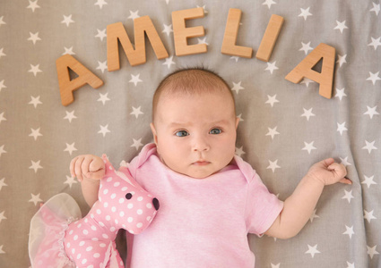 可爱的婴儿躺在床上的玩具和字阿米莉亚组成的木制字母。选择名称概念