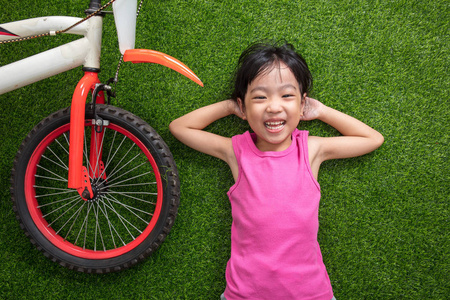 亚洲中国的小女孩躺在草地上与自行车