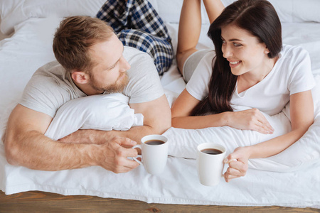 夫妇在床上喝杯咖啡放松的同时保持目光接触
