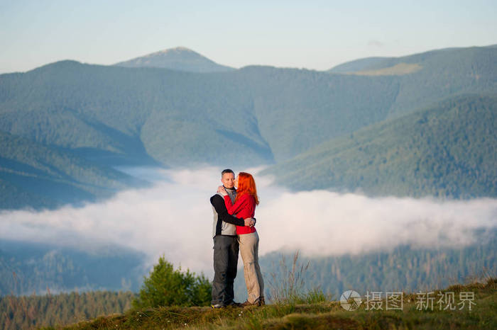 甜蜜情侣拥抱对美丽的山景观与早上岚在山区和森林.