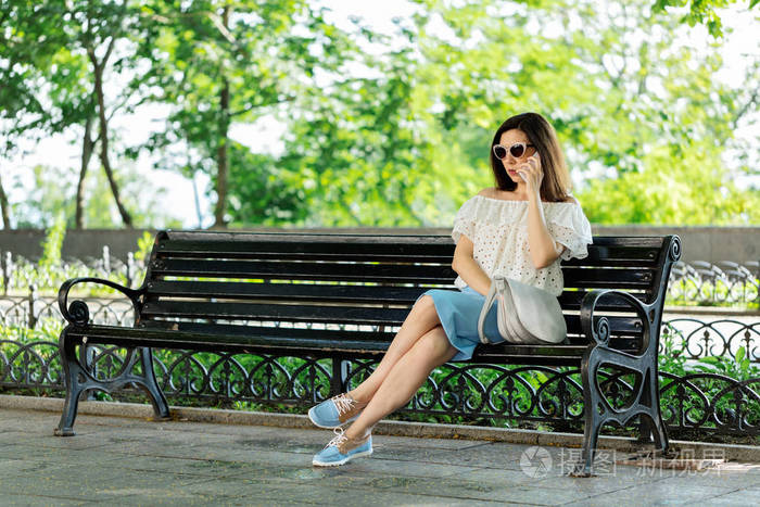 坐在一个公园里的白色上衣,蓝色裙子的年轻女子