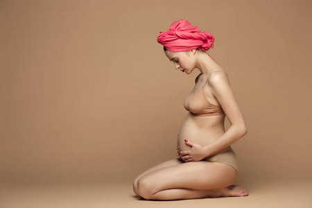 年轻美丽的孕妇坐在棕色背景