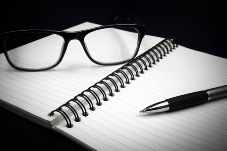 笔记本的眼镜和笔在黑色背景上