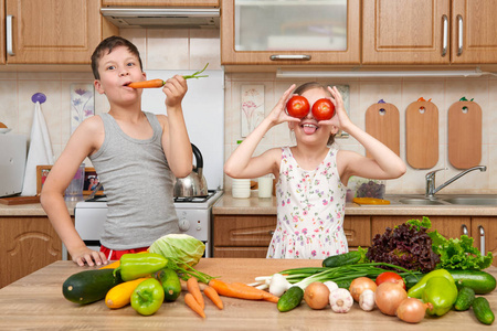 儿童女孩和男孩玩西红柿和胡萝卜，像双筒望远镜。家用厨房室内蔬菜和水果。健康食品的概念