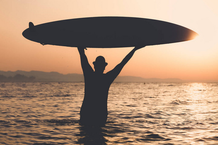 男人在日落时分缓缴海冲浪板的剪影