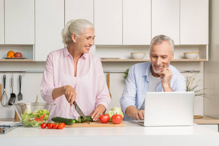 成熟爱的夫妇家庭使用的便携式计算机和烹饪沙拉
