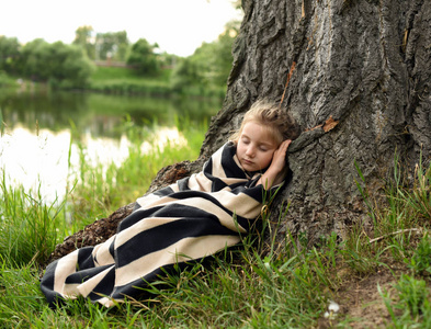 一个可爱的小女孩睡在一棵大树郁郁葱葱的绿色大自然下的一张照片