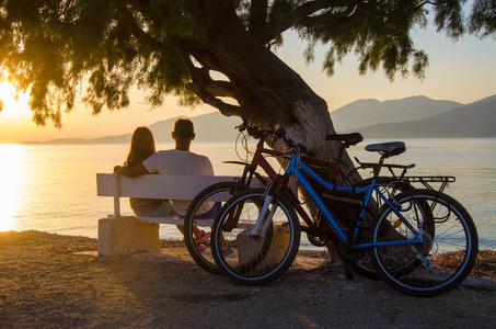 一对情侣看日落坐在海边的长椅上照片
