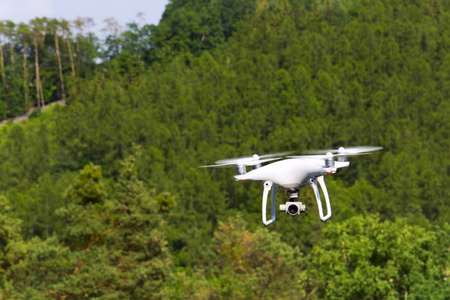 白色的无人驾驶直升机飞越森林的相机
